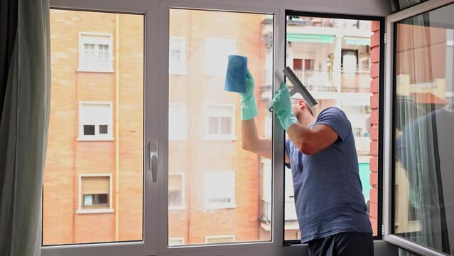 House cleaning. Caucasian man in rubber gloves cleans the glass of window using special foam and a blue napkin.