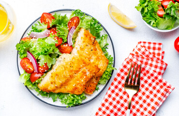 Fried white fish with salad from lettuce, cherry tomatoes and red onion with sesame seeds, white...