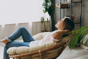 Side profile back view calm blonde young woman wearing casual clothes sit in armchair look camera...
