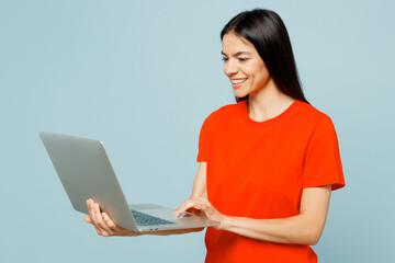 Side view young fun smiling IT latin woman she wear orange red t-shirt casual clothes hold use work...