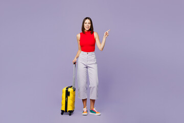 Traveler woman in red casual clothes hold suitcase point finger aside isolated on plain purple...