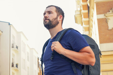 Fototapeta premium handsome bearded man with a backpack in the european center looks at the beautiful buildings, architecture, tourism. Tourism, summer vacation, backpack