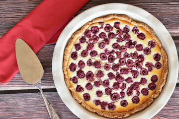 Homemade sour cream raspberry pie on wooden table. Baking dish, red napkin, metal cake shovel. Sweet pastry dessert, tasty food, vintage background.