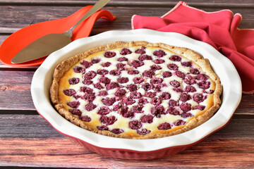 Homemade sour cream raspberry pie on wooden table, red and white baking dish, metal cake shovel, red napkin. Sweet pastry dessert, tasty food, vintage background.