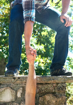 A person holding another person's hand pulling them up from below.