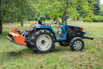 Mini-tractor with a chain mower chopping dry grass. Maintenance of the territory, mulching of grass.