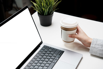 Hand holding drinking coffee cup with white screen laptop computer for mockup multimedia technology...