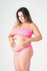 Obraz premium Happy plus size pregnant woman in pink underwear applying skin stretch mark cream on her belly on gray background, maternity clothes, pregnancy concept