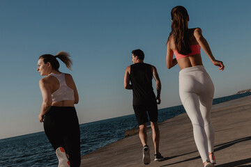 Rear view of three young people in sportswear enjoying morning jog seaside together © gstockstudio