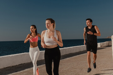Fototapeta premium Three confident young people in sportswear enjoying morning jog seaside together