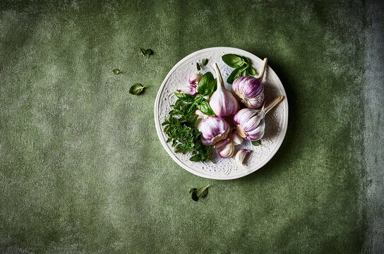 Garlic bulbs and fresh herbs on a ceramic plate. Culinary background. Top view
