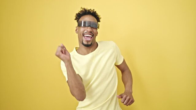 African american man using virtual reality glasses dancing over isolated yellow background