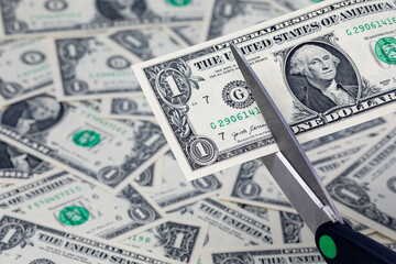 Scissors cutting a one dollar bill, cash money. Inflation, budget cuts and cost cutting concept.