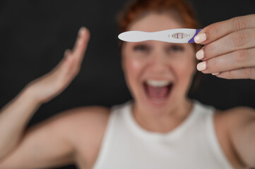 Blurred portrait of happy caucasian woman holding positive express pregnancy test on black...