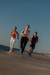 Three young people in sportswear looking concentrated while running seaside together