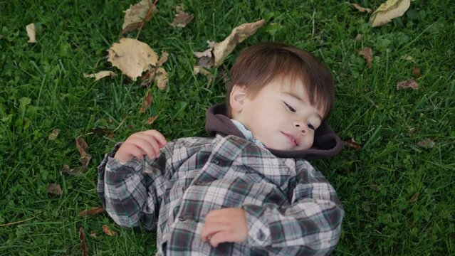 Happy asian kid lies on the grass and autumn leaves