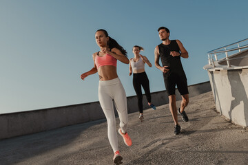 Three confident young people in sportswear looking concentrated while running outdoors together © gstockstudio