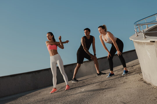 Three young people in sportswear warming up before training outdoors together