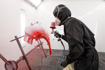 Auto painter spraying red paint on car fender in special booth. Painting vehicle parts at car...