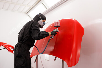 car painter paints the hood of the car in the spray booth in red
