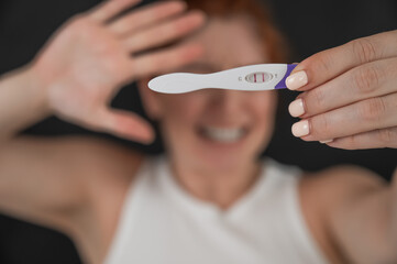 Blurred portrait of upset caucasian woman holding positive rapid pregnancy test on black background. 