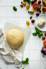 Step by step process of vegetable focaccia baking. Ball of homemade dough and fresh colorful tomatoes, peppers, basil and mozzarella on white tile background.