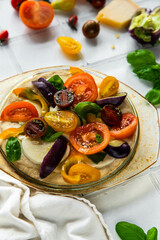 Step by step process of making colorful vegetable and mozzarella  focaccia bread. Focaccia topped with variety of tomatoes, peppers and mozzarella slices in glass baking form on white surface.