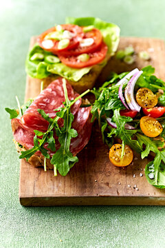 Freshly prepared sandwiches with veggies and salami on wooden chopping board
