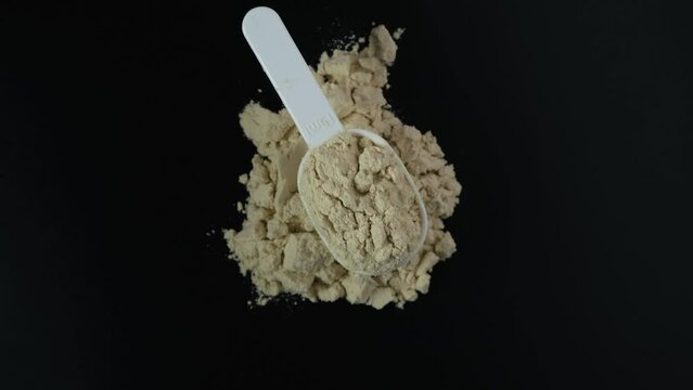 Pile of Soy protein concentrate, isolated from soybean. Video, 4K. Rotating. Food additive, ingredient for fitness cocktail or smoothie. Pure Plant Protein in white measuring spoon.