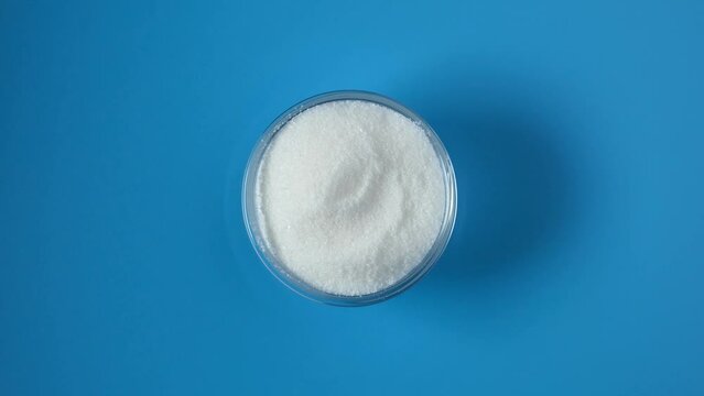 Sodium citrate powder on glass bowl on blue background, top view. Food additive E331, preservative and flavoring. Its properties are similar to Calcium Citrate (E333).