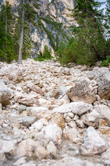 Mountain stream flowing into Braies lake surrounded by pine forests and the rocky ranges of the Dolomites in cloudy day, Italy.