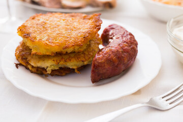 Potato pancakes with fried sausage on white plate