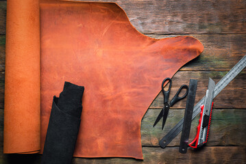 Leather pieces and leather craft work tools on the old wooden workbench background.