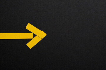 Yellow arrow made of paper on black background, copy space