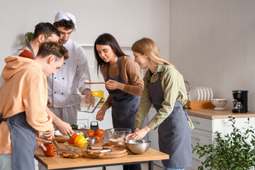 Italian chef with group of young people preparing pizza during cooking class in kitchen
