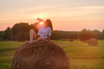 Happiness is found in the simplicity of nature as a woman sits on a hay bale during sunset....