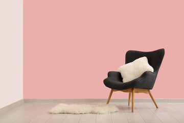 Grey armchair with cushion near pink wall