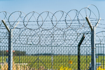 Security fence with barbed wire stretches across an open field during daylight