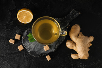 Glass cup of ginger tea with lemon and mint on black background