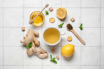Cup of ginger tea and bowl with honey on white tile background