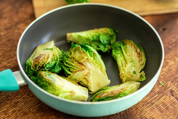 Lettuce halves toasted in a frying pan on a wooden background.