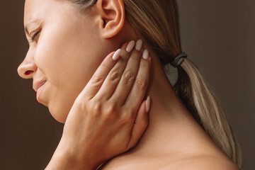 Profile of a young attractive caucasian blonde woman with a neck pain holding her neck near the...