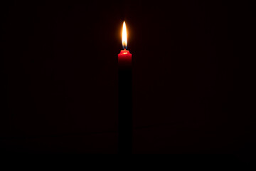 Single burning candle flame or light glowing on a small red candle on black or dark background on table in church for Christmas, funeral or memorial service with copy space. - Powered by Adobe