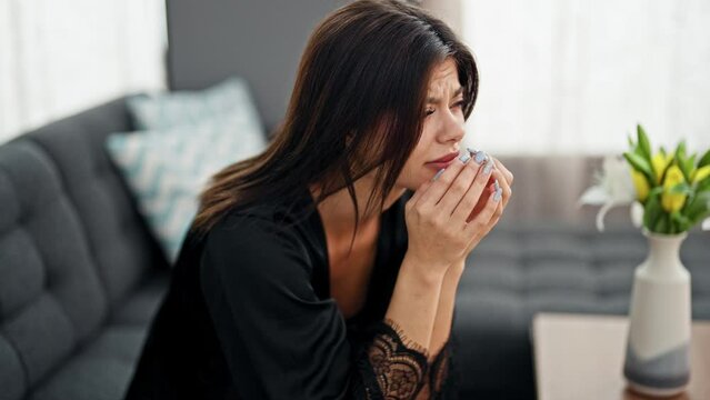 Young caucasian woman wearing dressing gown sitting on sofa stressed at home