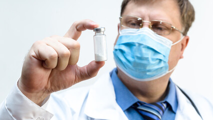 A doctor in a mask carefully looks tests in a test tube, the concept of biotechnology.