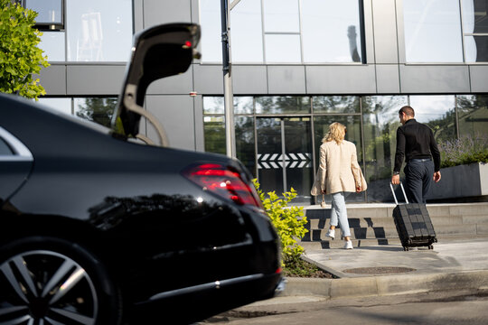 Chauffeur helps a businesswoman to carry her suitcase into a building, walking together, luxury taxi in front. Concept of business trips, idea of a luxury car transfer service © rh2010