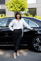 Full body portrait a beautiful woman in formal wear as a driver of luxury taxi stands near car on a...