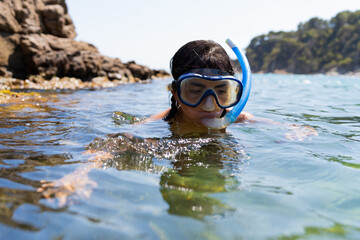 Beautiful latin woman enjoying a day of snorkeling on a rocky beach with beautiful an transparent waters on a bright summer day.