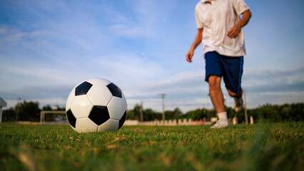 Obraz premium Action picture of sport player playing soccer football for exercise at green grass field park under the sunset. Picture with copy space.