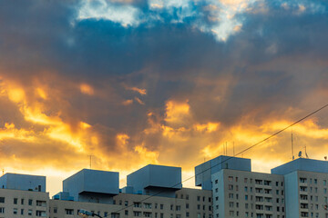 Beautiful cloudy sunset with sun hiding behind block of flats and highlighting sky in beautiful colors